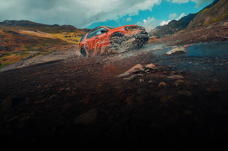 2026 Honda Passport TrailSport Elite in Sunset Orange front splashing through water on a rugged mountain trail (Mid-Size SUV).