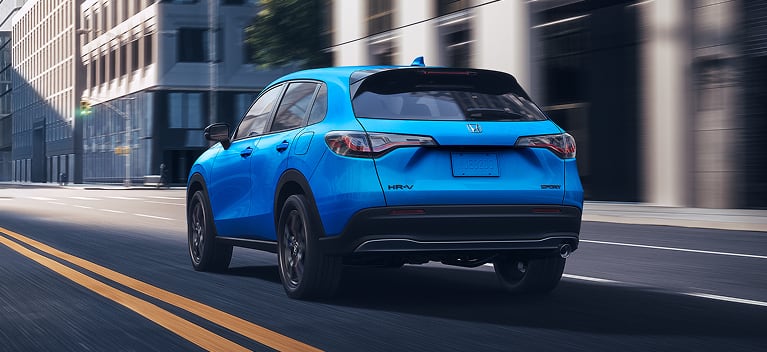 2027 Honda HR-V Sport in Boost Blue Pearl back driving on a city street (Subcompact Crossover SUV).